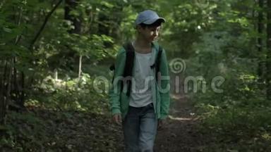 一个带背包的带着帽子的旅行男孩穿过树林四处张望